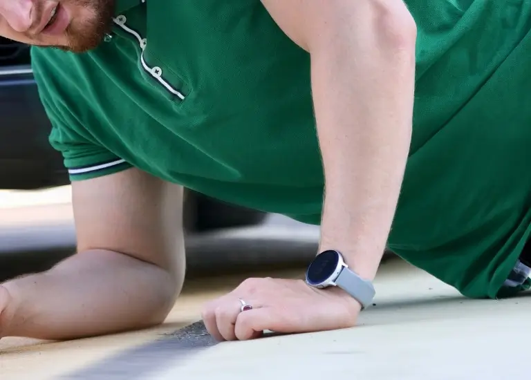a man in green shirt laying on the ground next to a car