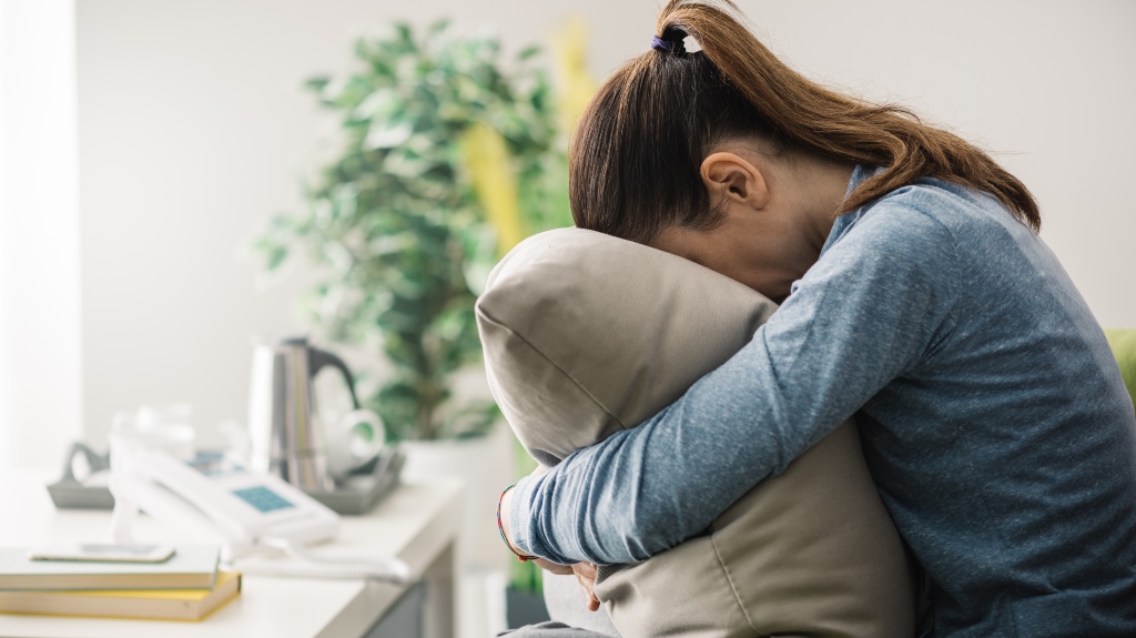 depressed woman sits on sofa and hides her face on pillow