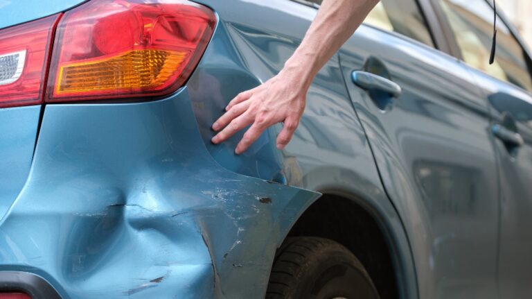 Driver hand examining dented car with damaged fender