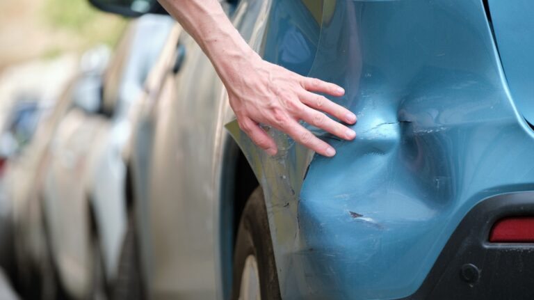 Driver hand examining damaged parked car